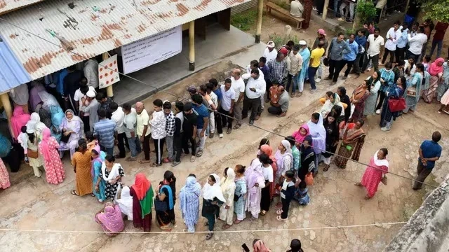 मतदान केंद्र पर वोट डालते लोग, लंबी कतारों में खड़े मतदाता और सुरक्षा व्यवस्था का दृश्य